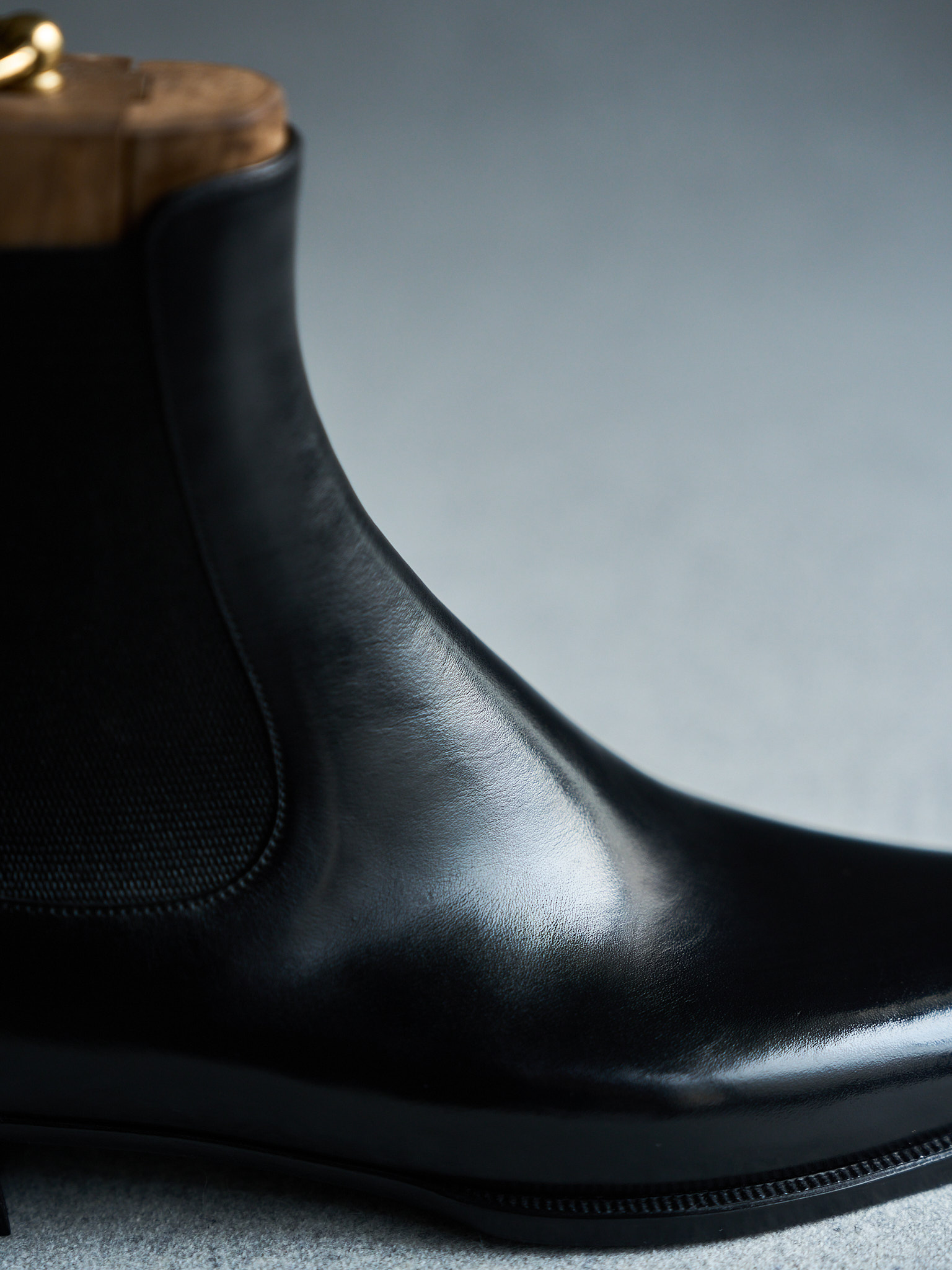Black leather Chelsea boot with wooden shoe tree on neutral background.