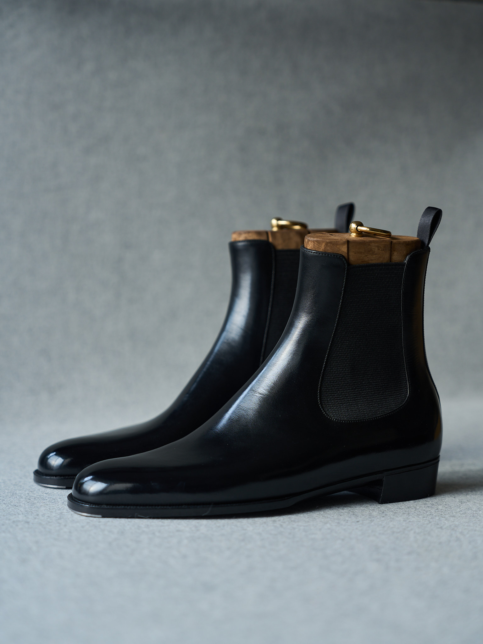 Black leather Chelsea boots with polished finish, wooden accents, and gold hardware details.