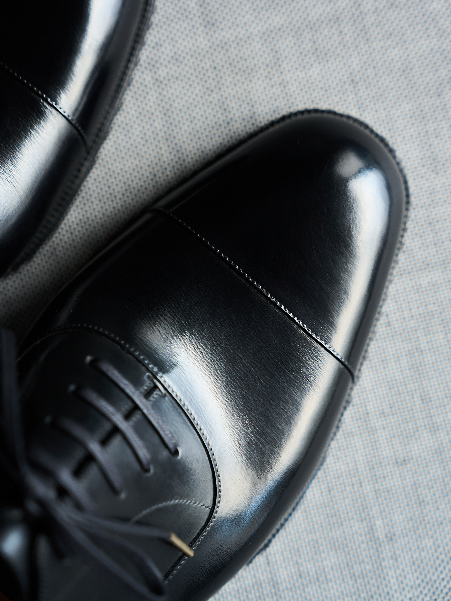 Polished black leather dress shoes with laces on a textured surface.