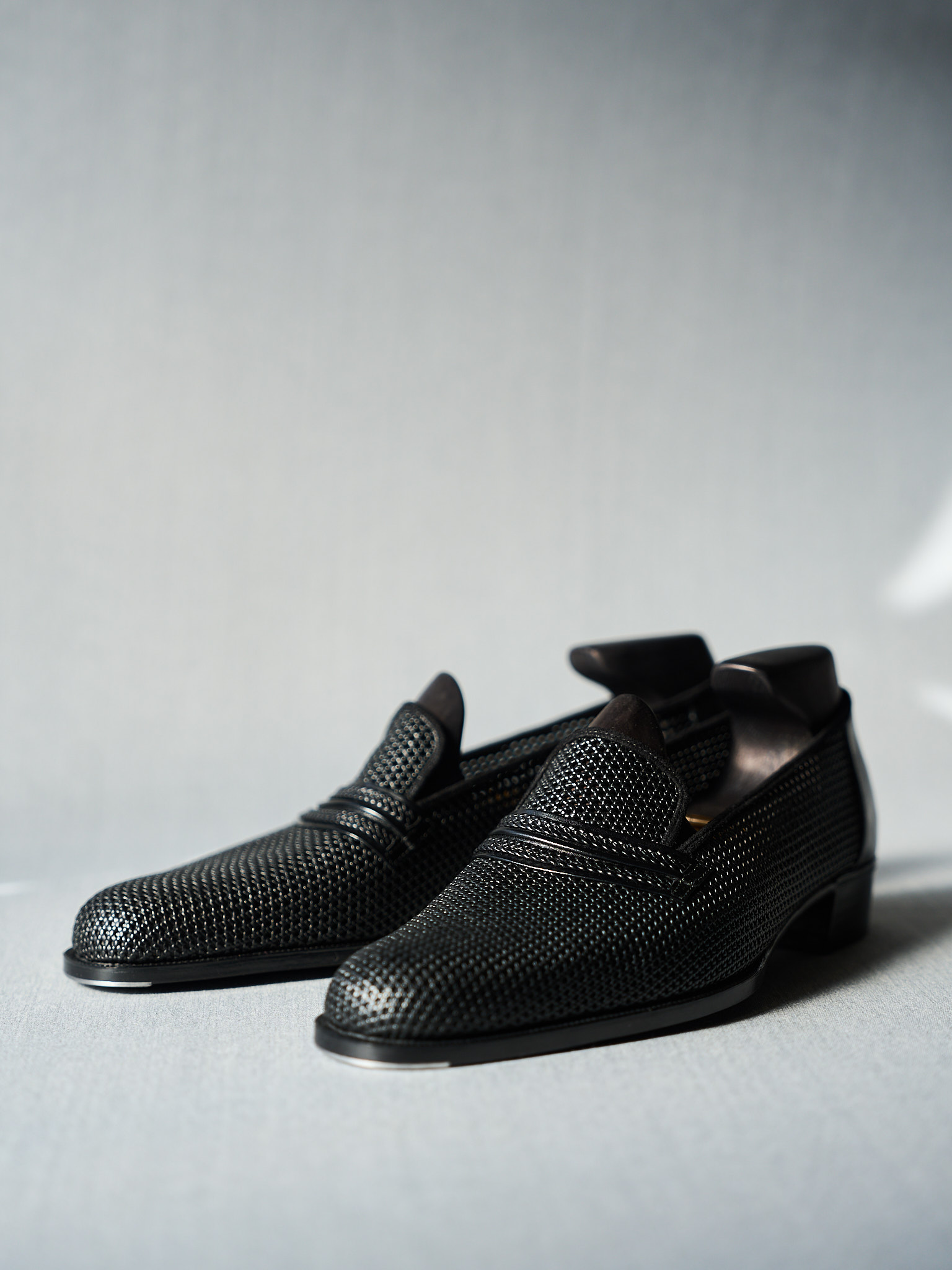Black perforated slip-on loafers for men with modern breathable mesh design.